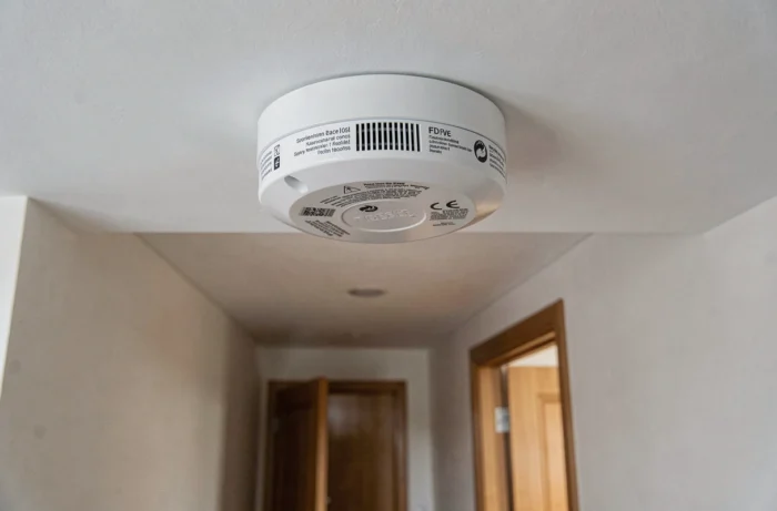 Détecteur de fumée blanc installé au plafond d'un couloir conforme au décret 2025-518